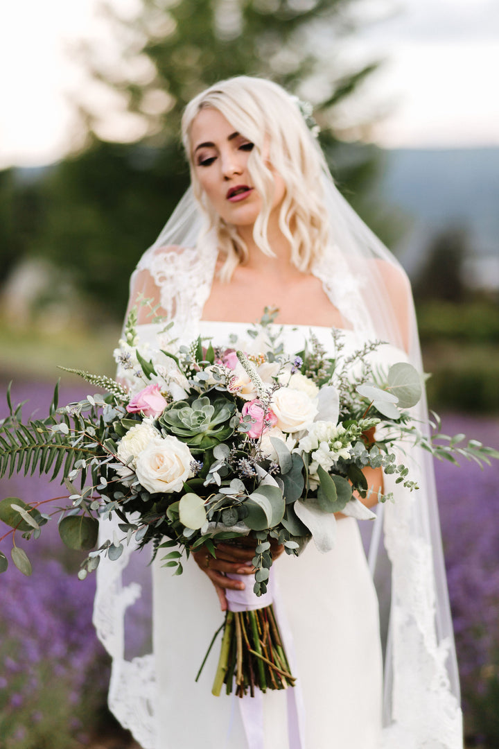 Bride wearing CASSANDRA lace veil outdoors with bouquet